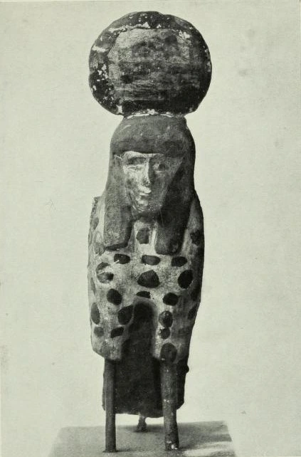 Black and white image of a bird with a human head and some massive sphere-shaped headgear on top. The hair goes up down to the chest at the sides, but is in line with the forehead at top.