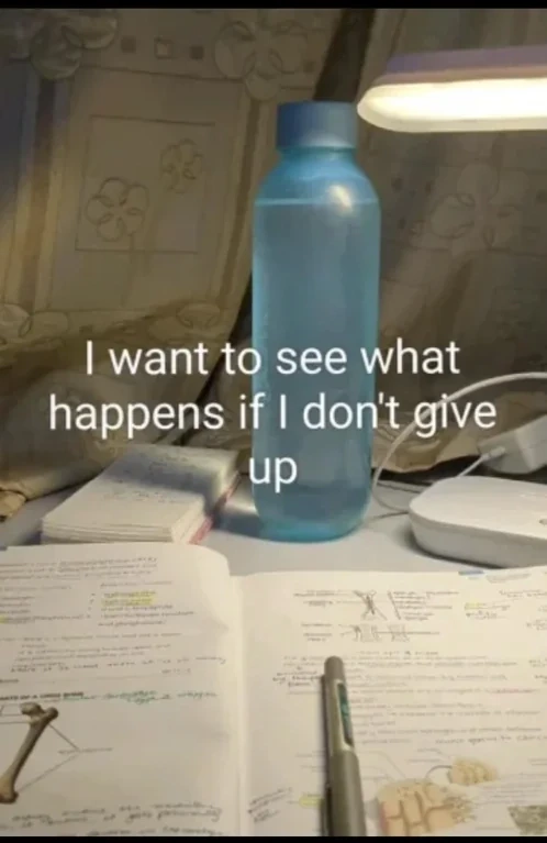 Textbook and water bottle on desk during late night study session. Text is overlayed "I want to see what happens if I don't give up"  